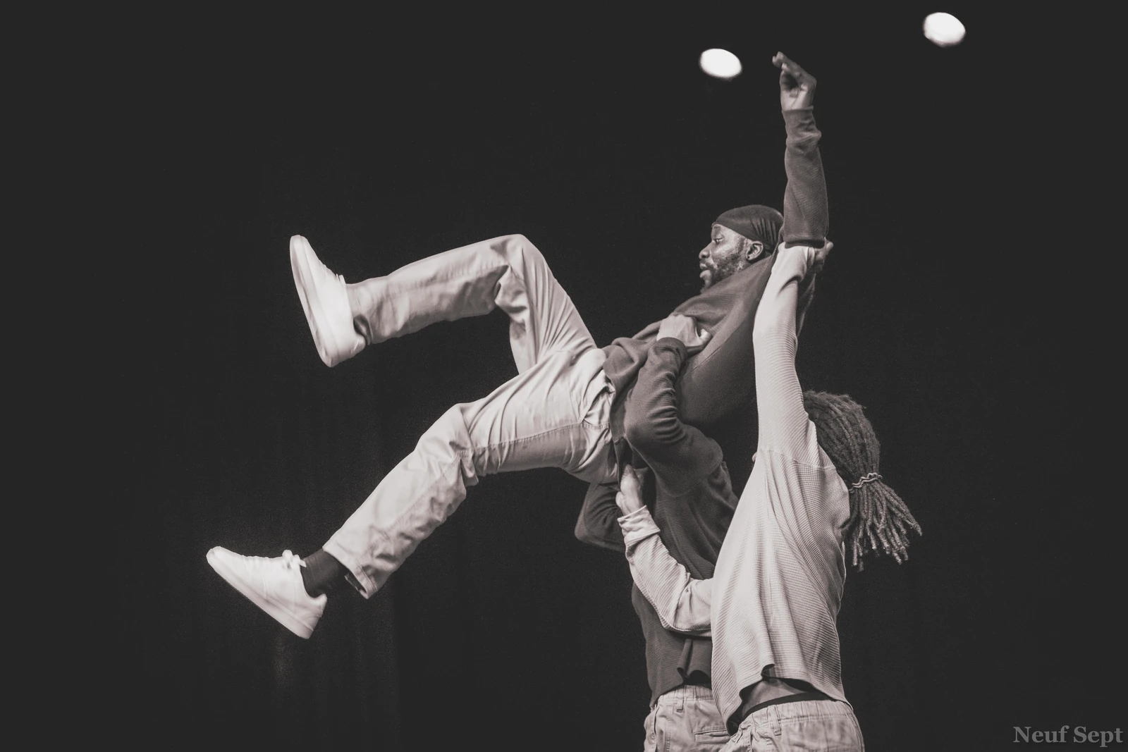 Un danseur soulevé au-dessus de ses partenaires, dans un mouvement collectif.